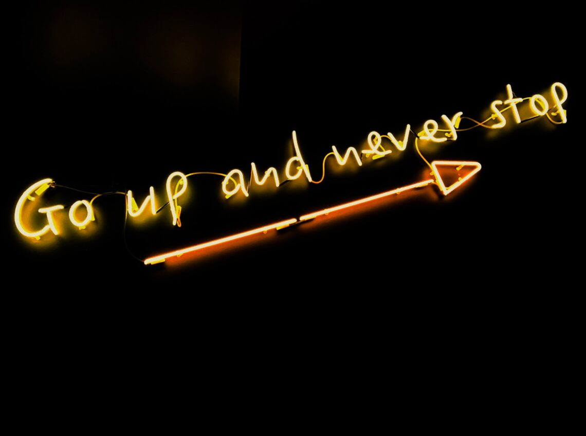 Go up and never stop neon letters with arrow on black wall
