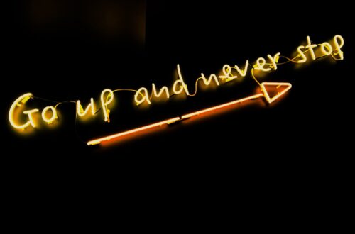 Go up and never stop neon letters with arrow on black wall
