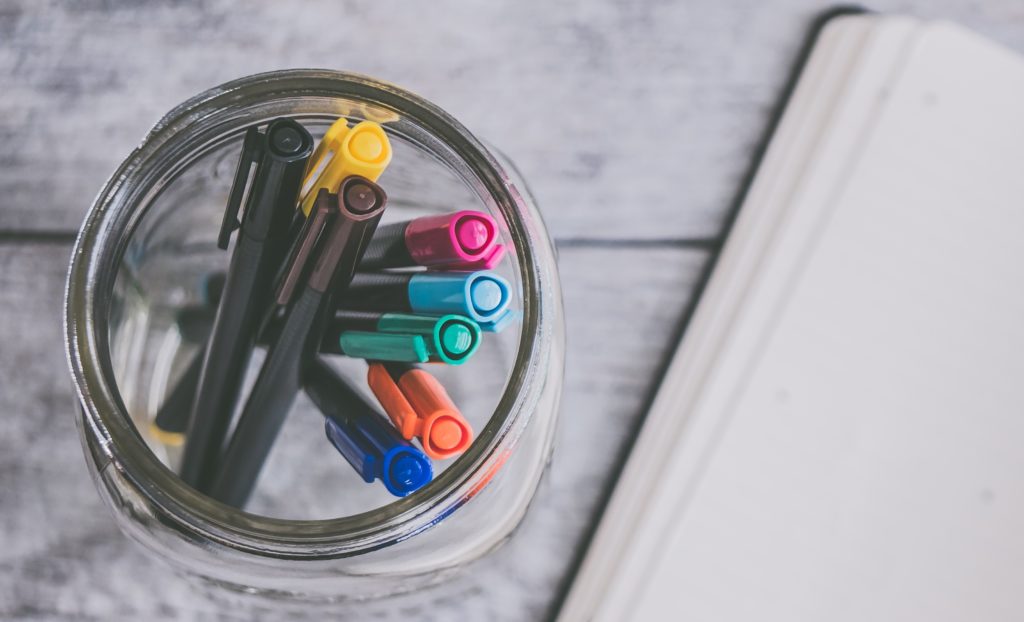 A jar of pens with coloured tops on a table
